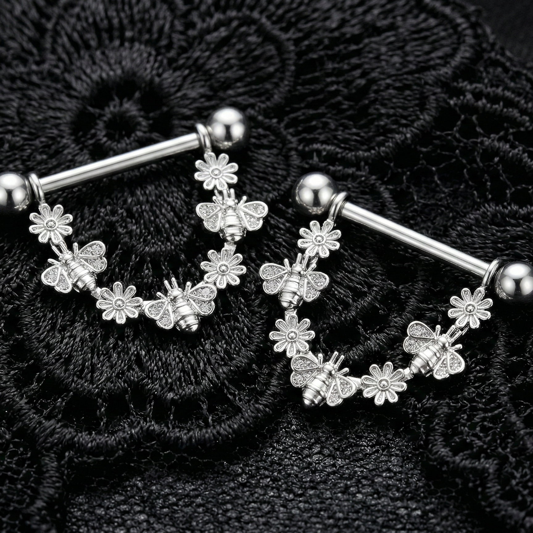 Silver floral nipple bars with bees charms on a black lace background