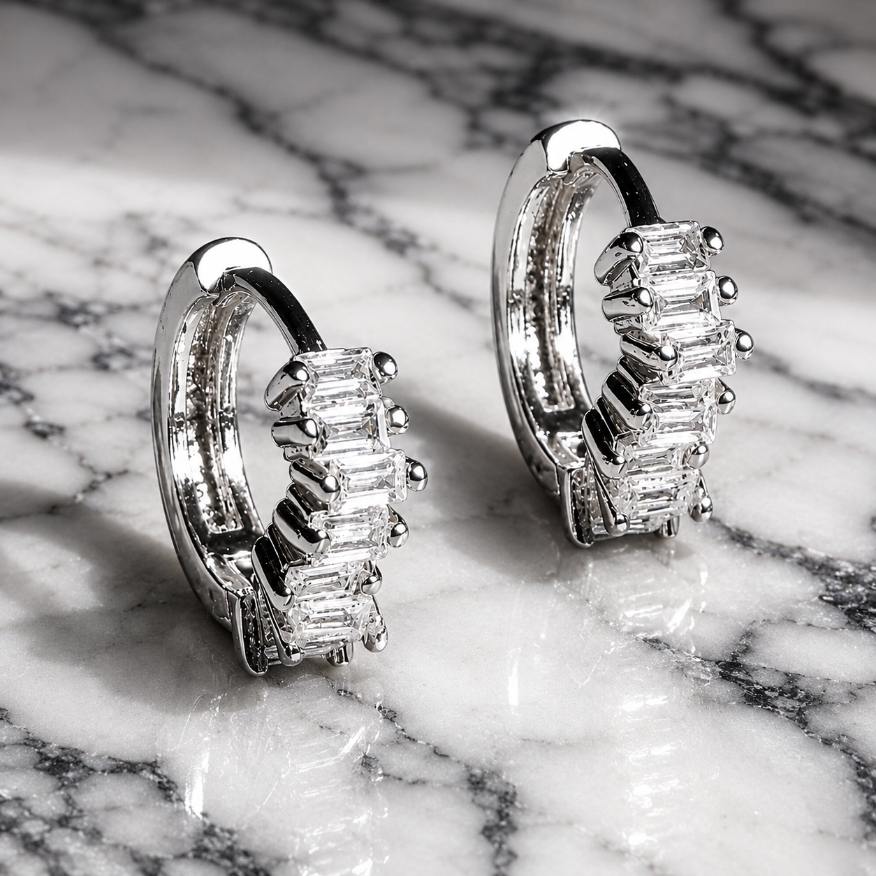 Silver hoop earrings with baguette cut gemstones on a marble surface