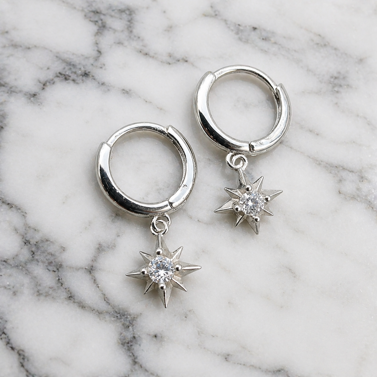 Silver hoop earrings with star-shaped diamond pendants on a marble background