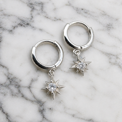 Silver hoop earrings with star-shaped diamond pendants on a marble background