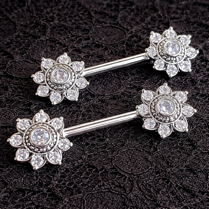 Silver mandala nipple bars with floral designs on a black lace background