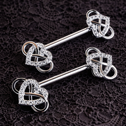 Silver nipple barbells with heart-shaped ends on a dark textured background