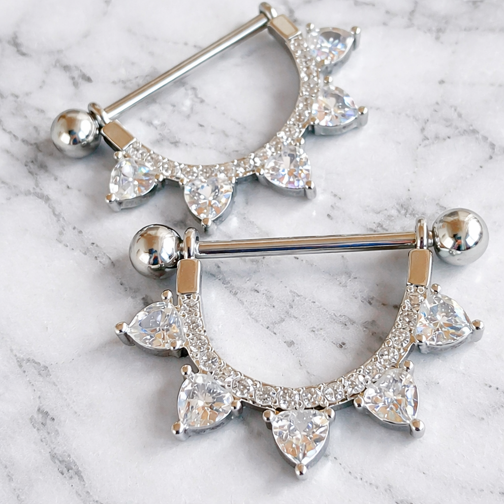 Silver nipple bars with clear gemstones on a marble background