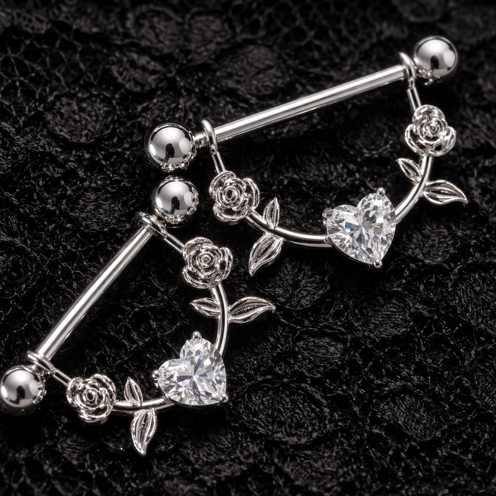 Silver nipple piercing bars with floral and heart designs and crystals on a black textured background