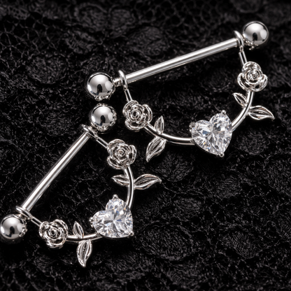 Silver nipple piercing bars with floral and heart designs and crystals on a black textured background