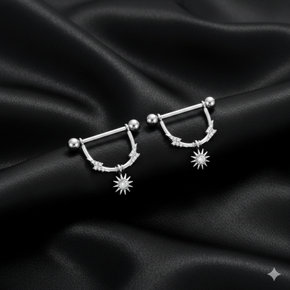 Silver nipple piercing shields with star designs on a black satin background