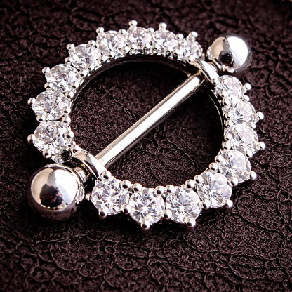 Silver nipple ring with clear gemstones on a dark textured background