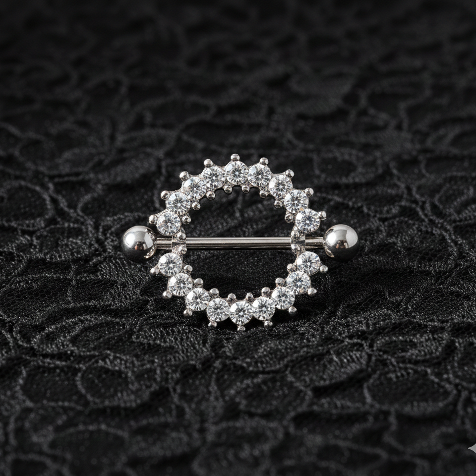 Silver nipple ring with embedded stones on a textured black background