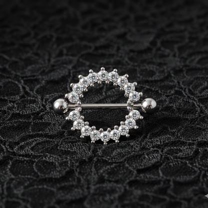 Silver nipple ring with embedded stones on a textured black background