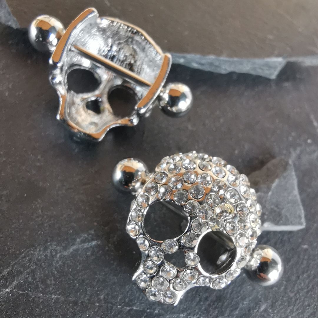 Skull-shaped silver nipple bar shields with diamond details, made with durable 16G surgical steel 316L