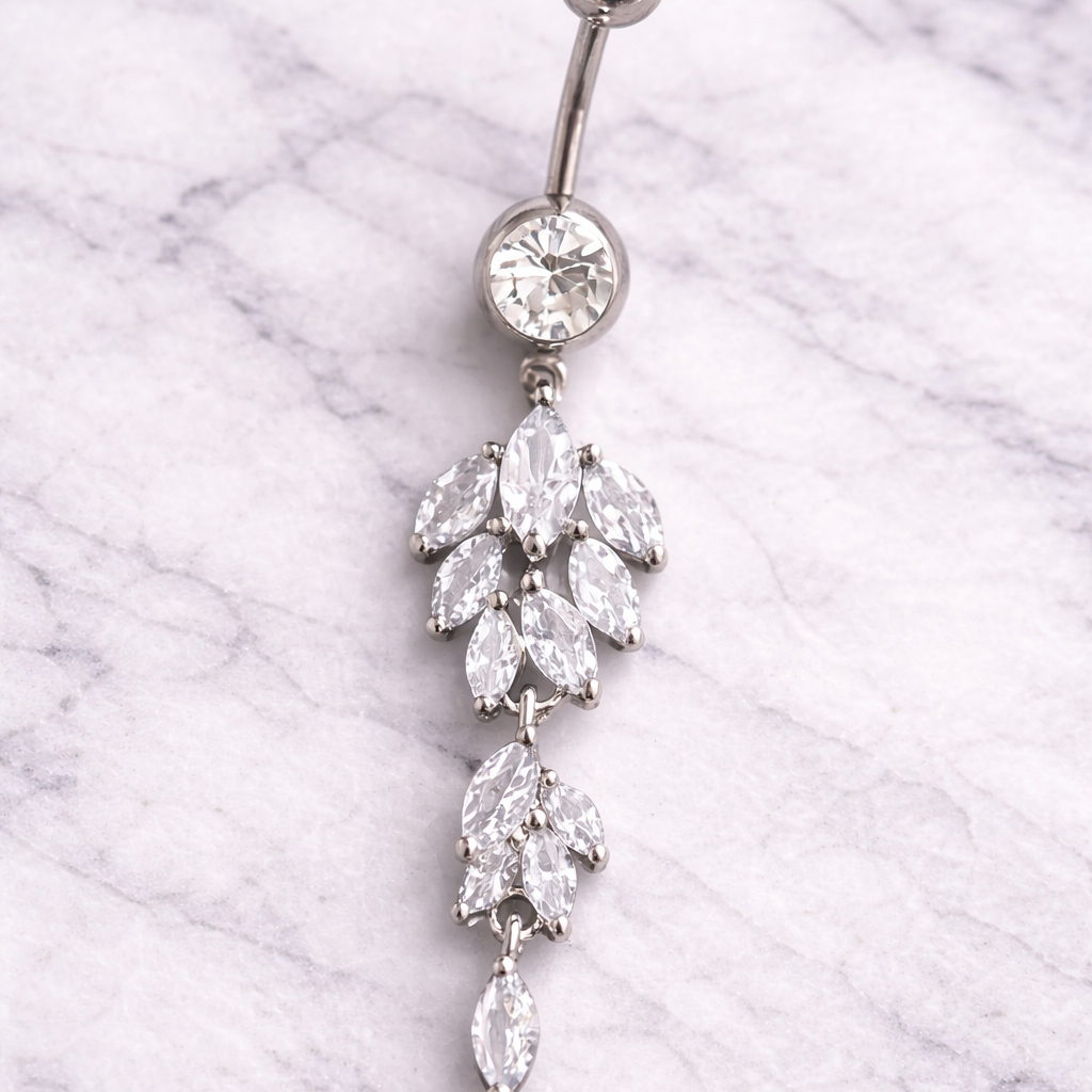 Silver belly button ring with crystal dangling earrings on a marble background