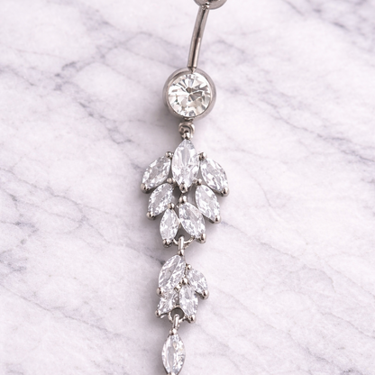 Silver belly button ring with crystal dangling earrings on a marble background
