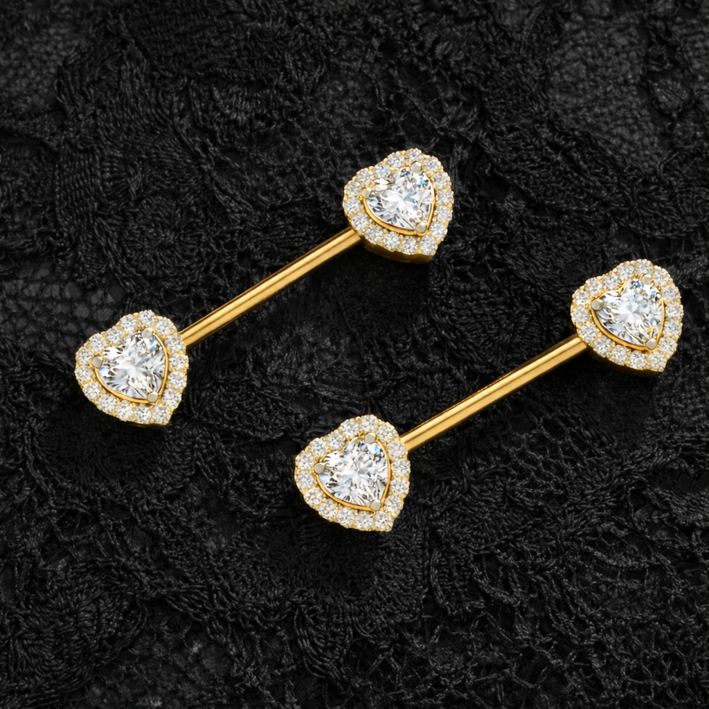Two gold barbell-shaped nipple piercing with heart-shaped gemstones on a black textured background.