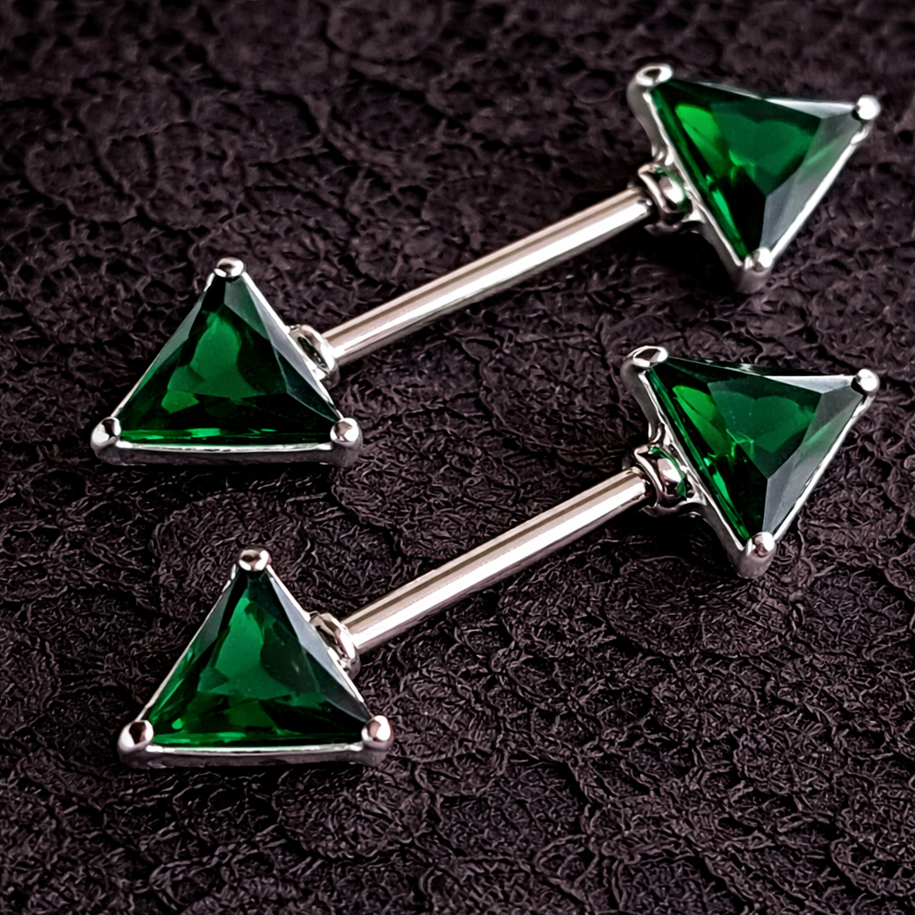 Two green triangle gem nipple rings on a dark textured background