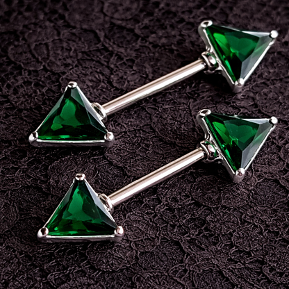 Two green triangle gem nipple rings on a dark textured background