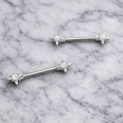 Two nipple silver barbell earrings with star-shaped ends on a marble background