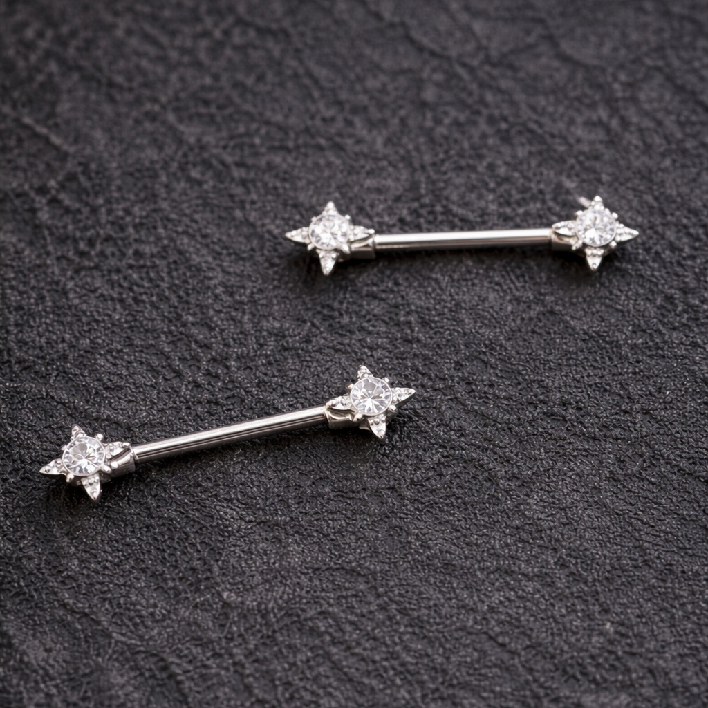 Two nipple silver bars with star designs on a dark textured surface