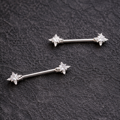 Two nipple silver bars with star designs on a dark textured surface