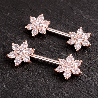 Two rose gold nipple bars with floral designs on a dark surface