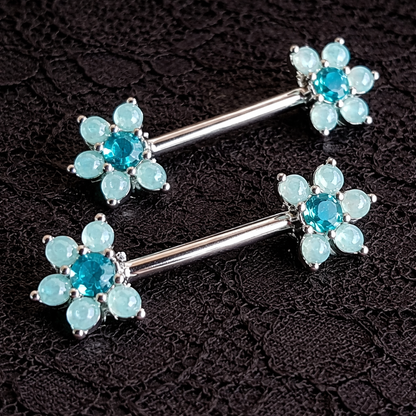 Two silver floral nipple rings with blue gemstones on a dark background