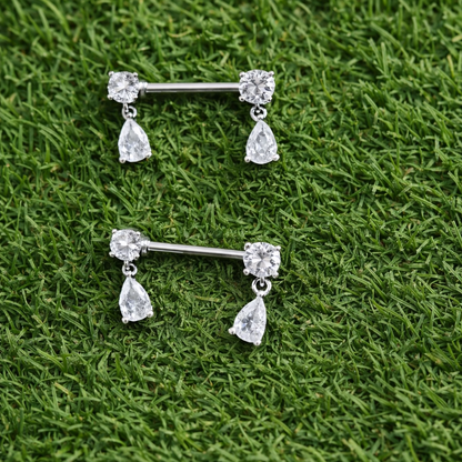 Two silver nipple barbells with teardrop-shaped gemstones on a grass background