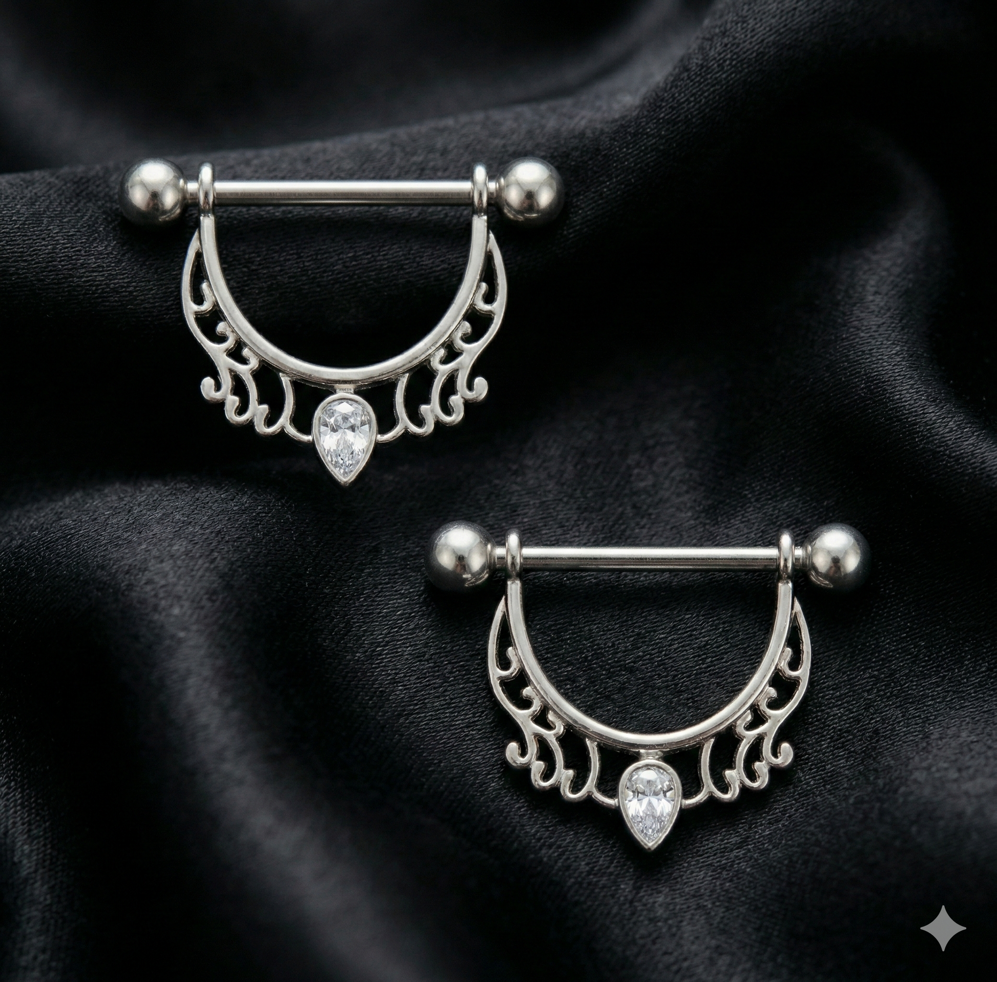 Two silver nipple bars with decorative designs on a black fabric background
