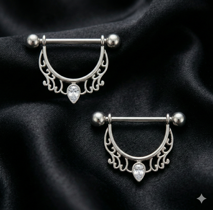 Two silver nipple bars with decorative designs on a black fabric background