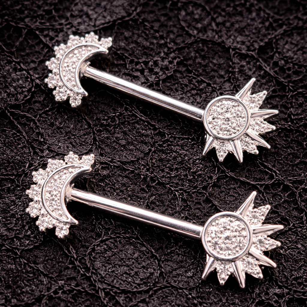 Two silver nipple bars with moon and sun designs on a black textured background.