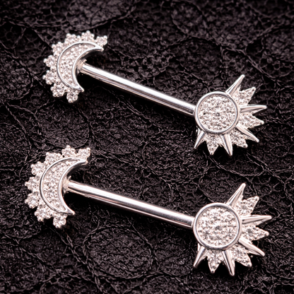 Two silver nipple bars with moon and sun designs on a black textured background.