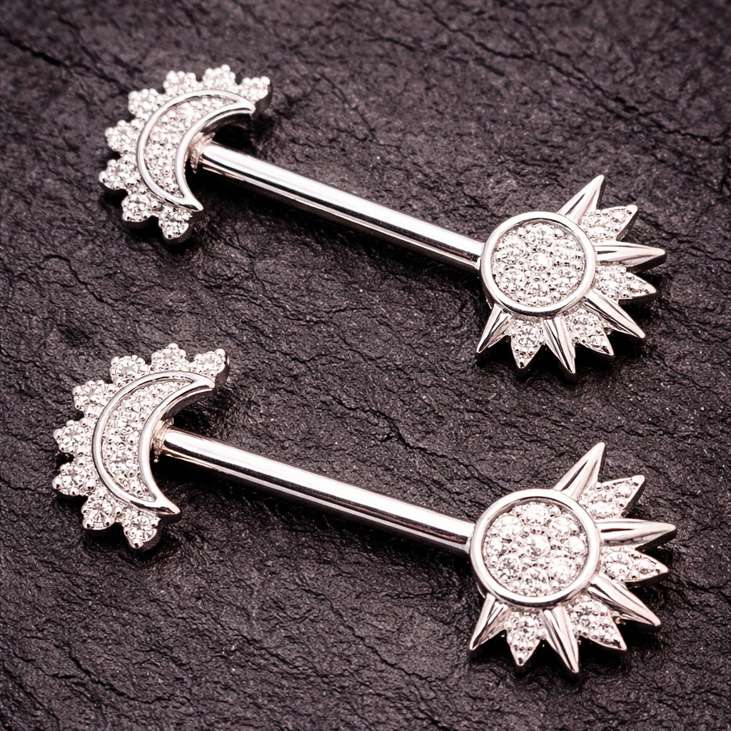 Two silver nipple bars with sun and moon designs on a dark textured background