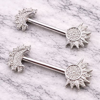 Two silver nipple bars with sun and moon designs on a marble background