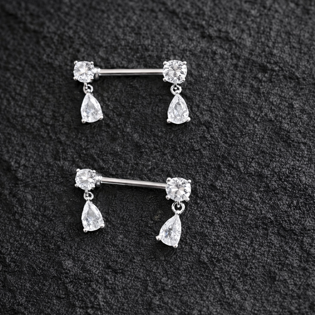 Two silver nipple bars with teardrop-shaped gemstones on a black textured background