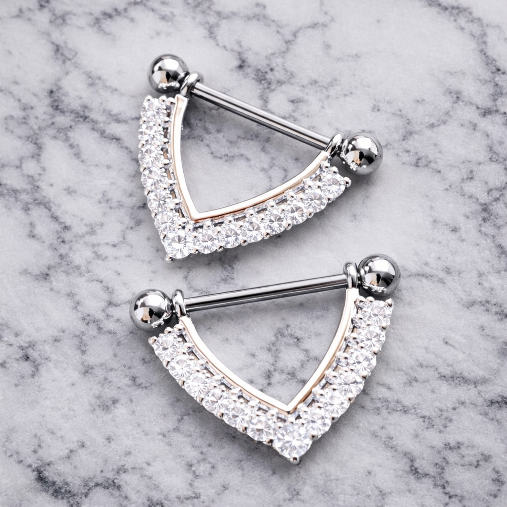 Two silver nipple piercing bars with clear gemstones on a marble background